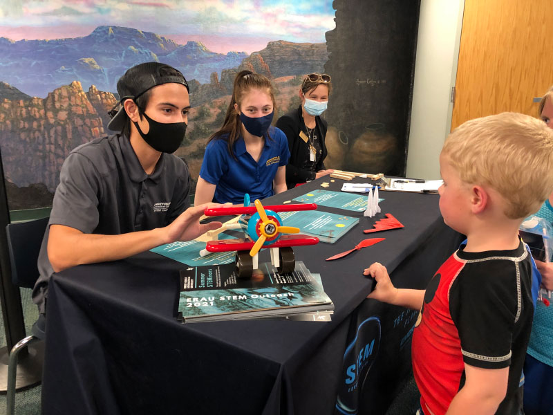 ERAU Students Kaleo Mendoza, Morgan Tollefson, and STEM Outreach Director Elise Anderson talk with Matthew Croy about the slingshot airplane STEM kit.